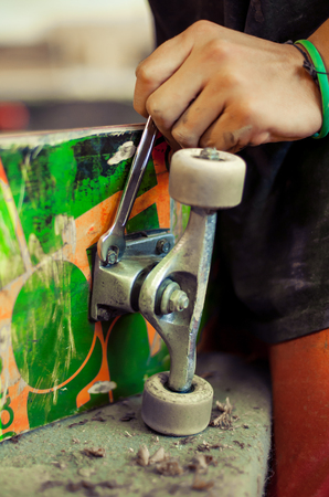 Young man in carpentry workshop fixing wheel on his skateboard. Close upの写真素材
