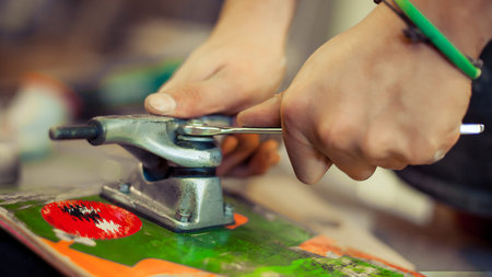 Young man in carpentry workshop fixing wheel on his skateboard. Close up