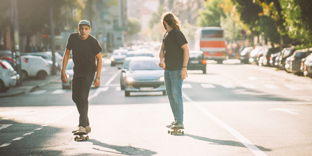 Two pro skateboard rider ride skate in front of the car on the city road street through traffic jamの写真素材