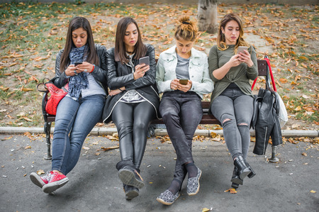 Group of girls using cellphones on park bench. Technology smartphones isolation and emotional depresion. Internet and social mediaの写真素材