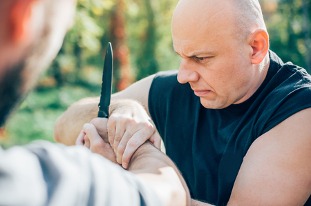 Kapap instructor demonstrates martial arts self defense knife attack disarming technique against threat and knife attack. Weapon retention and disarm training. Demonstration with a real metal knifeの写真素材
