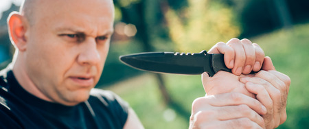 Kapap instructor demonstrates martial arts self defense knife attack disarming technique against threat and knife attack. Weapon retention and disarm training. Demonstration with a real metal knifeの写真素材