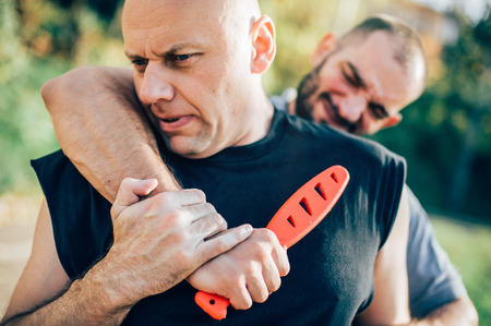 Kapap instructor demonstrates martial arts self defense disarming technique against threat and knife attack. Weapon retention and disarm training. Demonstration with plastic knifeの写真素材
