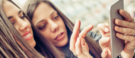 Two girl friends happy watching internet social media in smartphone. Close upの写真素材