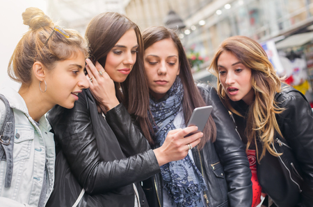 Happy four friends walking on the street and using cellphones. Internet and social mediaの写真素材