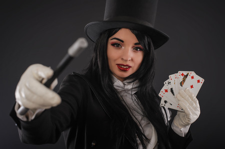 Pretty female magician dressed in performer costume suit with magic wand and playing cards. Studio shootの写真素材