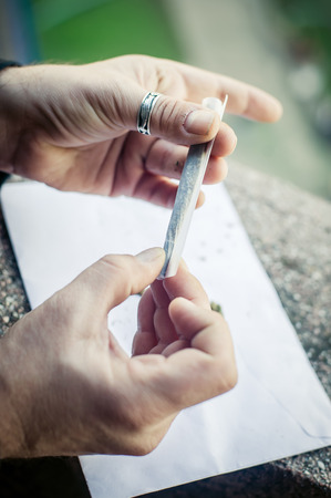 Preparing marihuana drug cigar. Rolling cannabis into paper with filter. Close upの写真素材