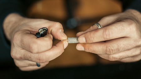 Preparing marihuana drug cigar. Rolling cannabis into paper with filter. Close upの写真素材