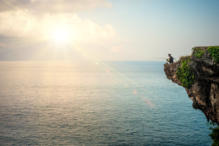 BALI, INDONESIA - 30. APRIL 2018. Man fishing on edge of cliff on the Indian coast. Day editorial shotのeditorial素材