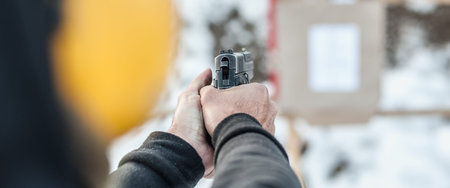 Detail back view of shooter holding gun in hand and shooting on target, close up. Shooting range