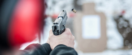 Detail back view of shooter holding gun in hand and shooting on target, close up. Shooting range