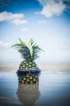 Fresh tropical exotic pineapple fruit with sunglasses on the beach. Water reflectionの写真素材