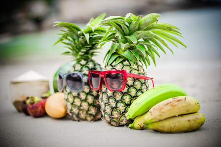Closeup of exotic and colorful tropical fresh fruit on the beach. Stylish pineapple with sunglassesの写真素材