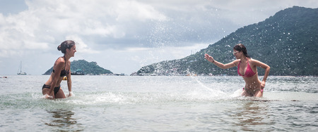 Best friends in bikini splashing water, having fun, playing together laughing on summer acationの写真素材