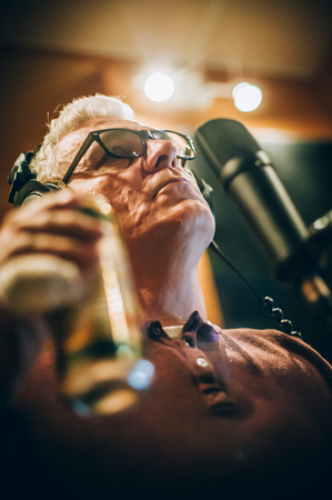 Behind the scene. Famous alternative male singer practice singing on the microphone in the messy recording music studio. Musician live singingの写真素材