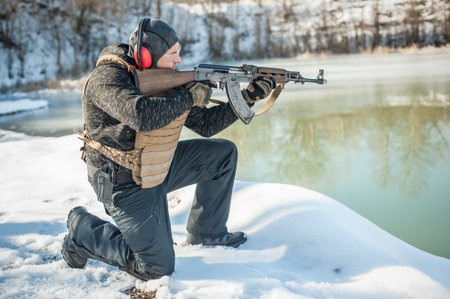 Army soldier in crouching position shooting from rifle machine gun on outdoor shooting range