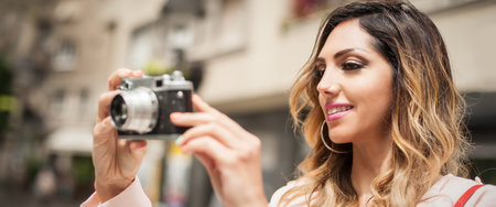 Beautiful young woman photographing with vintage film camera on the city street