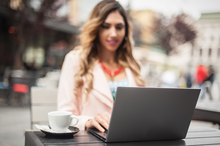 Young woman blogger freelancer in outdoor cafe with computer laptop, city street backgroundの写真素材