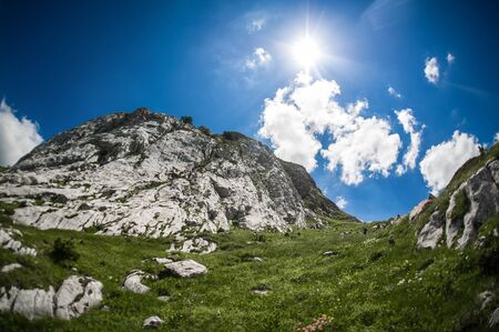 Mountain summer landscape. Meadow with huge stones among the grass on top of the hillside near the peak of mountain rangeの写真素材
