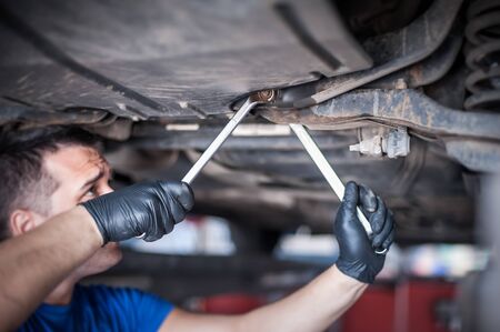 Master auto mechanic repairer service technician checking the condition under the car, on vehicle lift in workshopの写真素材