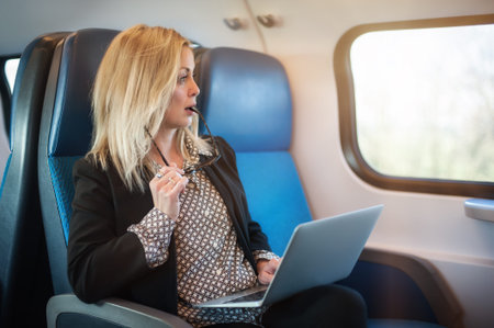 Beautiful woman traveling using laptop in train. Businesswoman pensive looking out the window while...