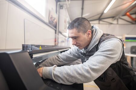 Electrical engineer operator repairs large premium industrial printer and plotter machine in digital printshop officeの写真素材