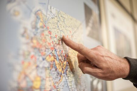 Close-up of hand and finger pointing, showing region and location on the geography or business topography navigation atlas map. Selective focusの写真素材