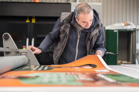 Worker printmaker technician operator works in large digital printing press hall and printshop...
