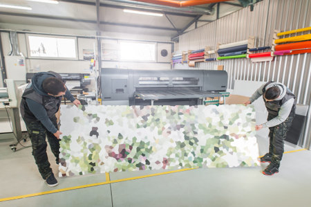 Two worker printmaker technician operator works in large digital printing press hall and printshop...