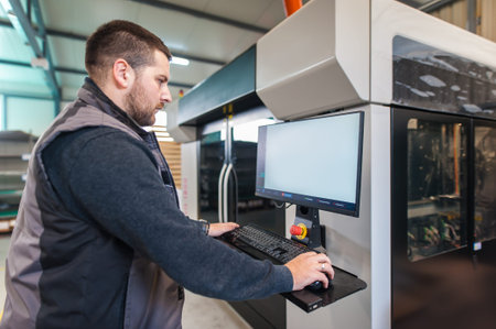 Printshop worker printmaker technician works on large modern 3d printer machine with computer...