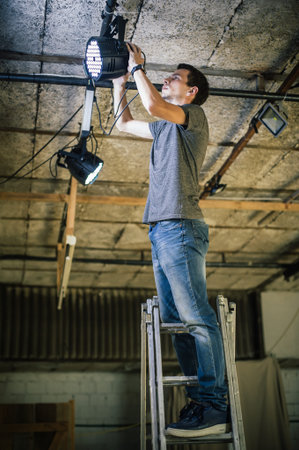 Theater lighting technician electric engineer adjusting focus of lighting elements backstage....