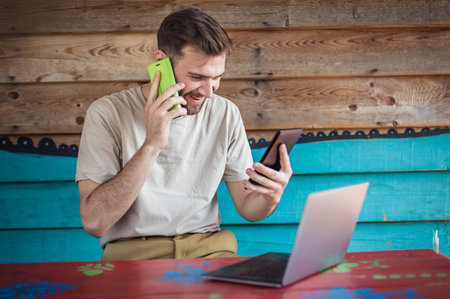 Young crazy hipster talking on the mobile smart phone, using tablet and looking on laptop. Internet...