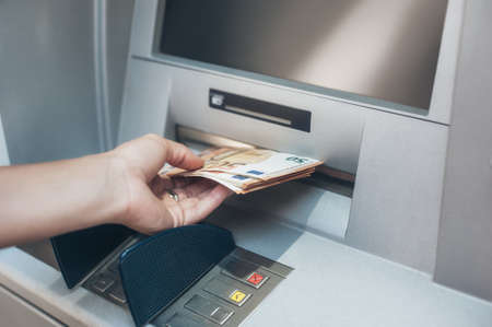 Woman hand taking money from bank cash ATM machine. Close up. Cash point. Finance, transactions, credit card, money withdraw, currency conceptの写真素材