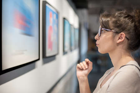 Young woman in modern art exhibition gallery hall contemplating artwork. Abstract paintingの写真素材