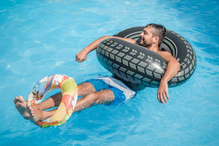 Portrait of happy young man floating on swimming pool with inflatable rings