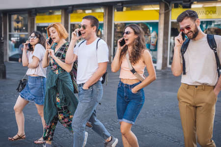 Alienation addiction. Group of friends walking and talking in the city center. Young people addiction to new technology trends. Youth, new generation internet friendship conceptの写真素材