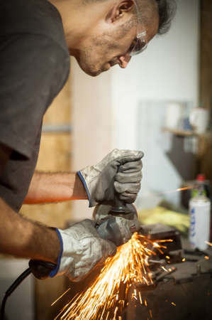 Man working with electric grinder tool on steel structure in factory, sparks flying. Grinding machine in actionの写真素材