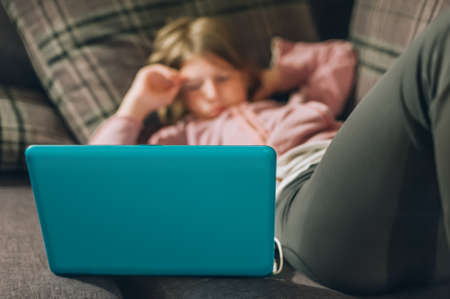 Teenage girl with laptop and casual clothes lying alone on soft couch and watching favorite series. Home, technology and internet conceptの写真素材