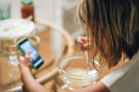 Teen girl eating breakfast in the kitchen while using her smart phoneの写真素材