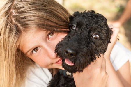 Cute smiling little girl playing with her dog, black poodle, in the tall green grass