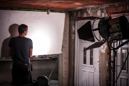 Behind the scene. Filmmaking lighting technician electric engineer adjusting reflector and setup lights diffusion intensity for movie film scene. Light Department. Film Crewの写真素材