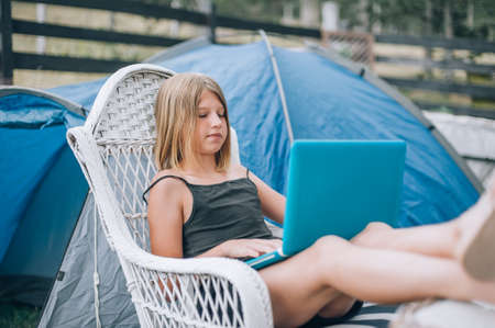 Portrait of beautiful focused girl sitting on a swing chair, using laptop and smartphone. Free time outdoorの写真素材