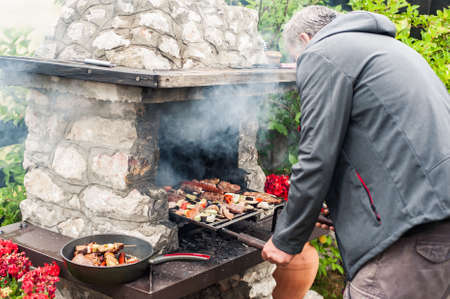 Man cooking meat on barbecue grill at bbq party in summer garden. Food, people and family time conceptの写真素材
