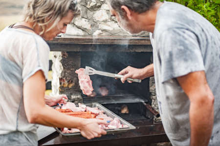 BBQ grilling party. Couple in garden making barbecue grill. Food, people and family time conceptの写真素材