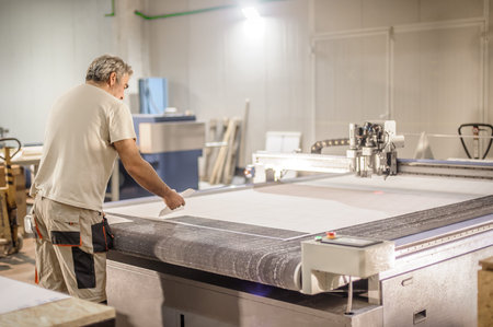 Factory worker technician works on large CNC digital cutter machine for cutting fabric textile...