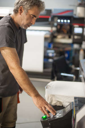 Professional graphic print technician work on digital t-shirt printing machine printer in printing production shopの写真素材