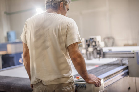 Factory worker technician works on large CNC digital cutter machine for cutting fabric textile...