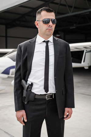 Professional male spy agent bodyguard with gun. Security police in civilian black suit with...