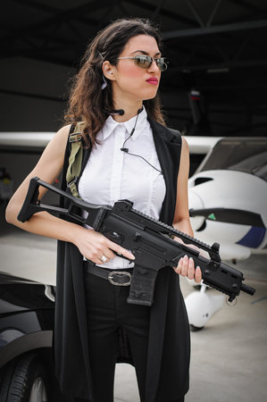 Beautiful professional female spy agent bodyguard posing with rifle submachine gun. Security police...