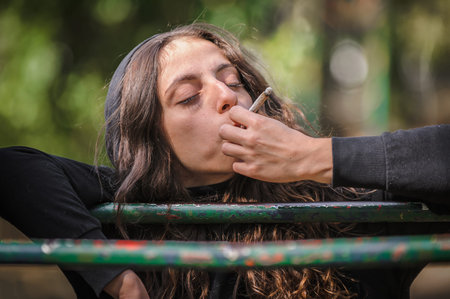 Closeup detail view of young woman smoke cannabis marijuana ganja or hashish joint cigarette. Casual female girl smoking thc green grass. Real life scene conceptの写真素材
